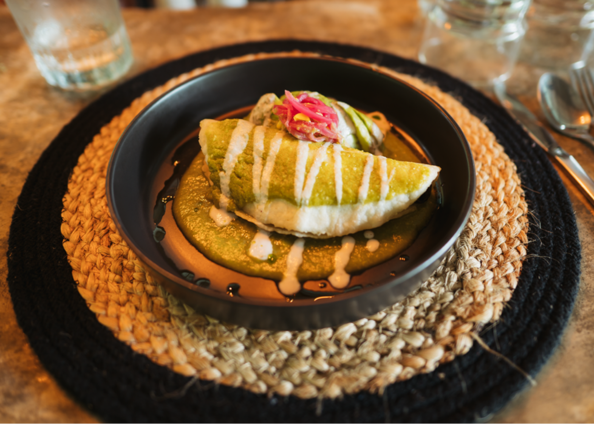 Empanada plated for dinner. Black plate, round black and tan placemat, water glasses, and silverware.
