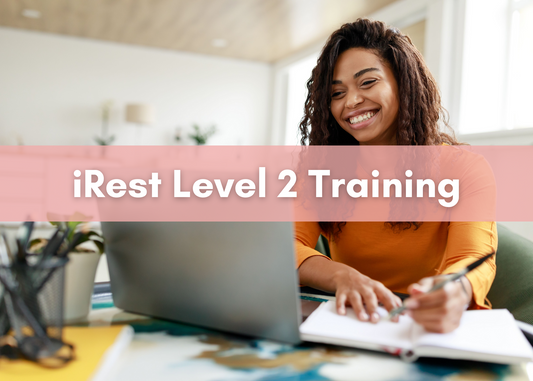 Smiling woman sitting at a desk with a laptop and notebook, studying online during iRest Level 2 Training
