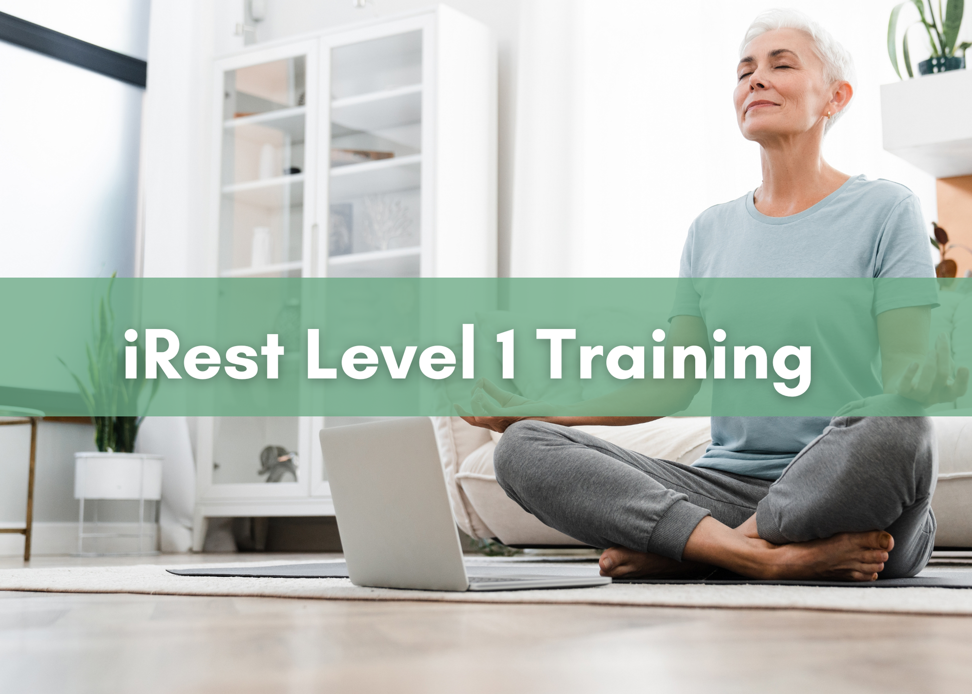 An older woman with short gray hair sits cross-legged on the floor in a bright, modern living room, eyes closed and smiling peacefully as she meditates in front of an open laptop. A green banner across the center reads “iRest Level 1 Training” in bold white text.